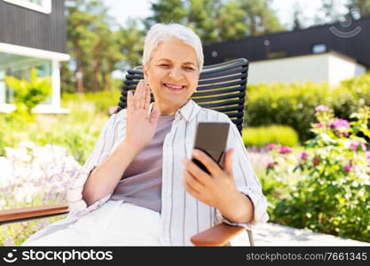 technology, old age and people concept - happy smiling senior woman with smartphone having video call and waving hand at summer garden. happy senior woman with phone having video call