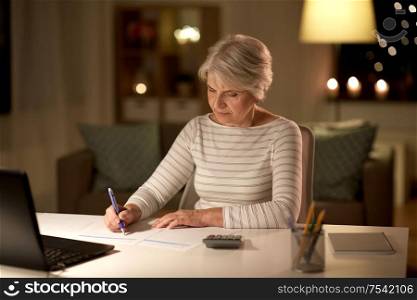 technology, old age and people concept - senior woman filling tax form at home in evening. senior woman filling tax form at home in evening