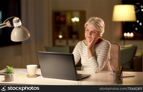 technology, old age and people concept - senior woman with laptop at home in evening. senior woman with laptop at home in evening