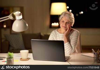 technology, old age and people concept - senior woman with laptop at home in evening. senior woman with laptop at home in evening