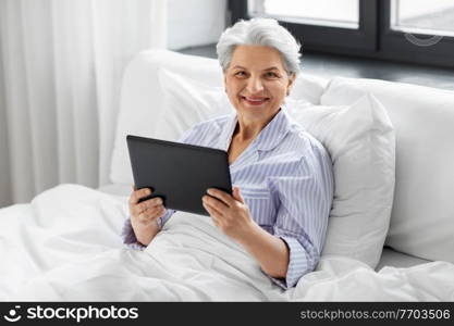 technology, old age and people concept - senior woman with tablet pc computer in bed at home bedroom. senior woman with tablet pc in bed at home bedroom