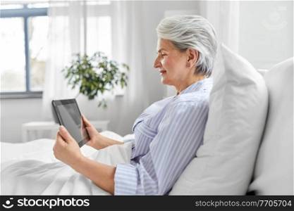 technology, old age and people concept - senior woman with tablet pc computer in bed at home bedroom. senior woman with tablet pc in bed at home bedroom