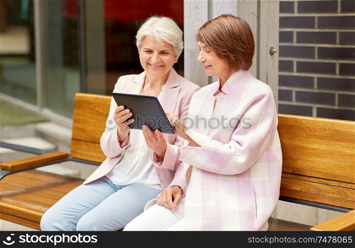 technology, old age and people concept - senior women with tablet pc computer sitting on street bench in city. senior women with tablet computer in city