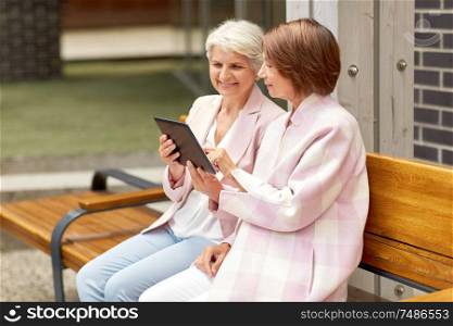 technology, old age and people concept - senior women with tablet pc computer sitting on street bench in city. senior women with tablet computer in city