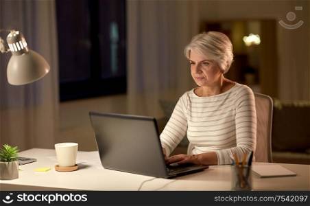technology, old age and people concept - serious senior woman with laptop at home in evening. senior woman with laptop at home in evening