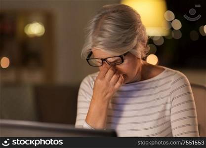technology, old age and people concept - tired senior woman in glasses with laptop working at home in evening. tired senior woman with laptop at home at night