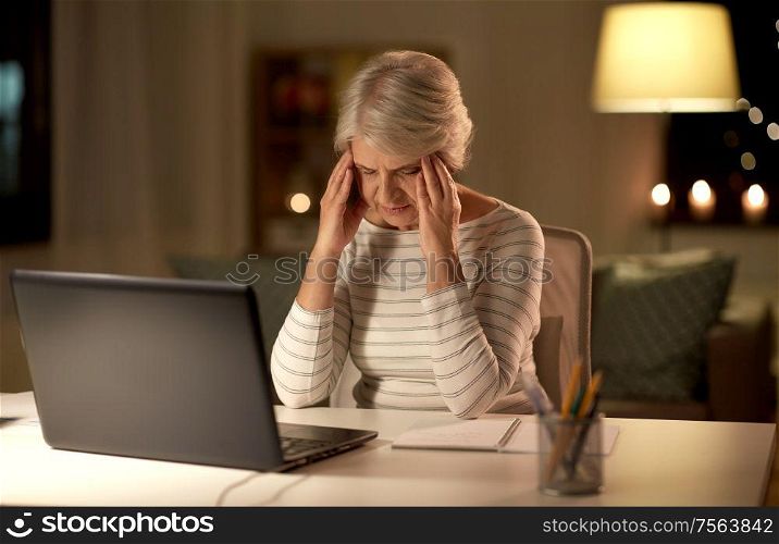 technology, old age and stress concept - tired or stressed senior woman with laptop computer having headache at home in evening. tired senior woman with laptop at home at night