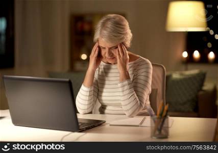 technology, old age and stress concept - tired or stressed senior woman with laptop computer having headache at home in evening. tired senior woman with laptop at home at night