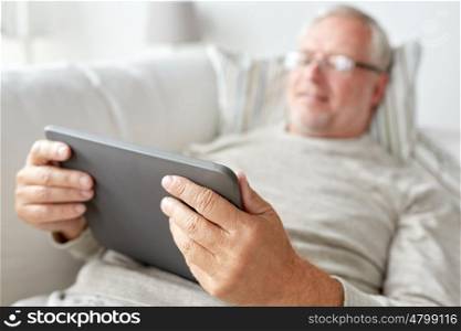 technology, old age, people and lifestyle concept - happy smiling senior man with tablet pc computer lying on sofa at home