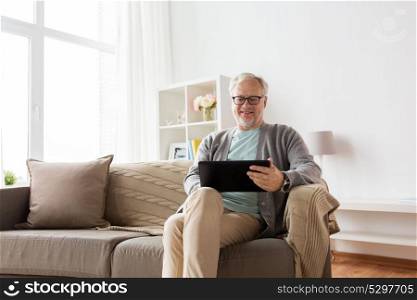 technology, old age, people and lifestyle concept - happy smiling senior man with tablet pc computer sitting on sofa at home. senior man with tablet pc sitting on sofa at home