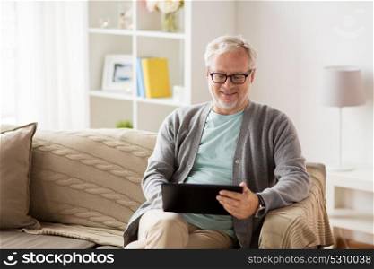 technology, old age, people and lifestyle concept - happy smiling senior man with tablet pc computer sitting on sofa at home. senior man with tablet pc sitting on sofa at home