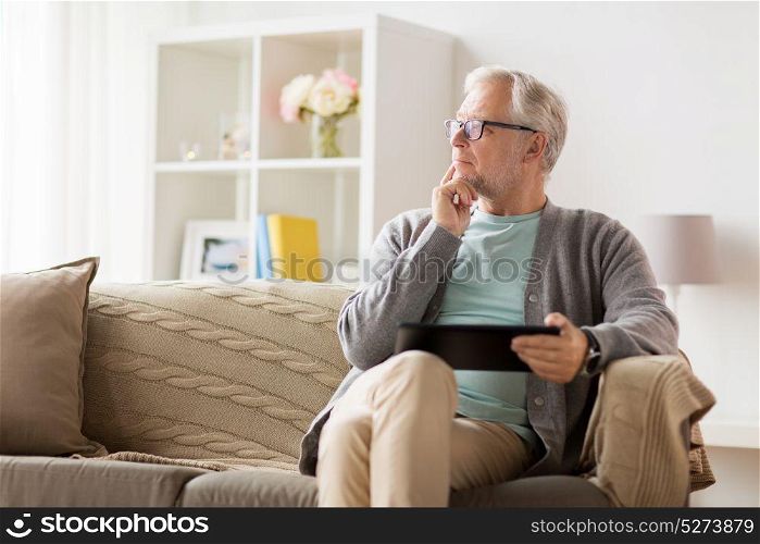 technology, old age, people and lifestyle concept - senior man with tablet pc computer sitting on sofa at home and thinking. senior man with tablet pc sitting on sofa at home