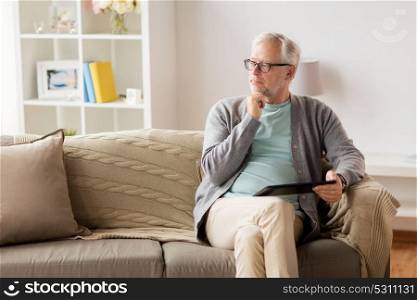 technology, old age, people and lifestyle concept - senior man with tablet pc computer sitting on sofa at home and thinking. senior man with tablet pc sitting on sofa at home