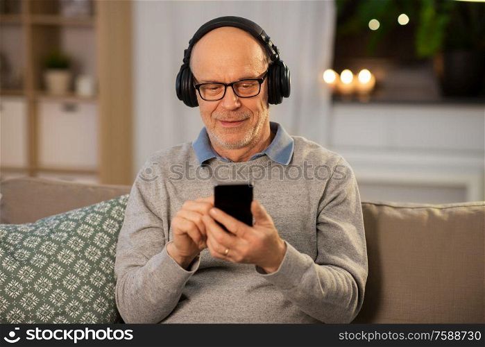technology, old people and lifestyle concept - happy senior man with smartphone and headphones listening to music at home in evening. senior man with smartphone and headphones at home