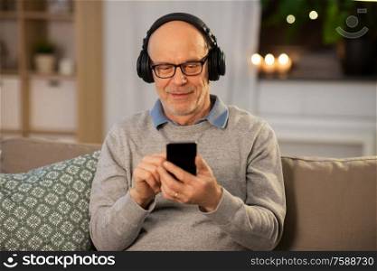 technology, old people and lifestyle concept - happy senior man with smartphone and headphones listening to music at home in evening. senior man with smartphone and headphones at home