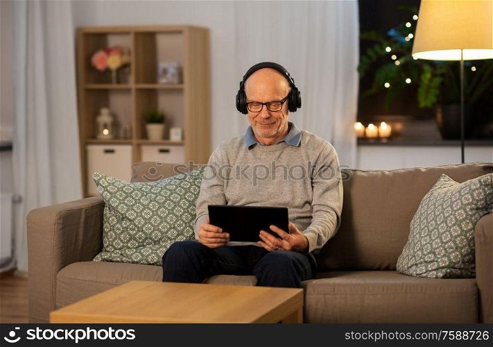 technology, old people and lifestyle concept - happy senior man with tablet pc computer and headphones listening to music at home in evening. senior man with tablet pc and headphones at home