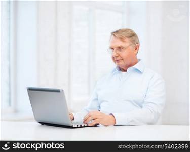 technology, oldness and lifestyle concept - old man in eyeglasses working with laptop computer at home