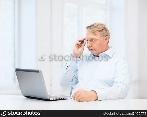 technology, oldness and lifestyle concept - old man in eyeglasses working with laptop computer at home