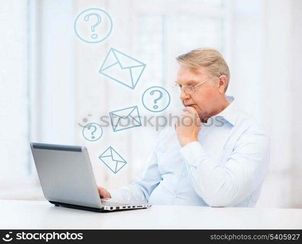 technology, oldness and lifestyle concept - old man in eyeglasses working with laptop computer at home