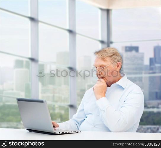 technology, oldness and people concept - senior man in eyeglasses with laptop over office window background