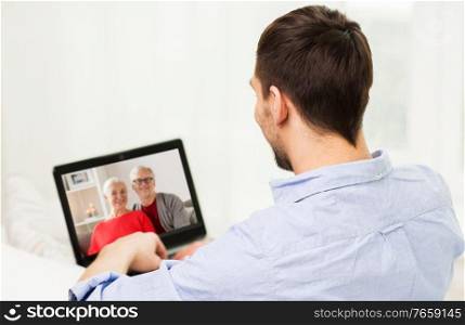 technology, online communication and self isolation concept - young man having video call with his family on laptop computer at home on christmas. man with laptop having video call with his family