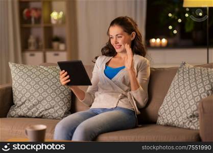 technology, online communication, internet and people concept - smiling young woman with tablet pc computer having video call at home in evening. woman with tablet pc having video call at home