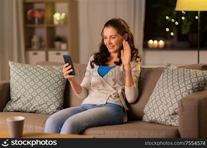 technology, online communication, internet and people concept - smiling young woman with smartphone having video call at home in evening. woman with smartphone having video call at home