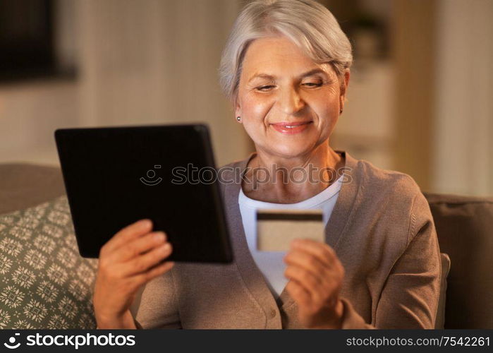 technology, online shopping, age and people concept - happy senior woman with tablet pc computer and credit or bank card at home in evening. old woman with tablet pc and credit card at home