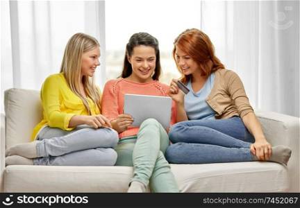 technology, online shopping and internet banking concept - three smiling teenage girls or friends with tablet pc computer and credit card at home. teenage girls with tablet pc and credit card