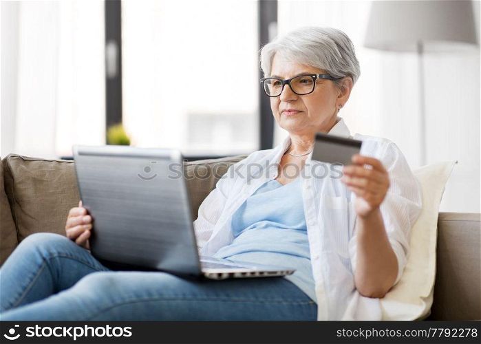 technology, online shopping and people concept - happy senior woman in glasses with laptop computer and credit or bank card at home. senior woman with laptop and credit card at home