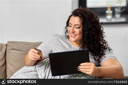 technology, online shopping and people concept - happy smiling woman with tablet pc computer and credit card on sofa at home. woman with tablet pc and credit card at home