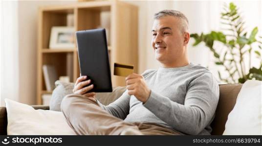 technology, online shopping, people and lifestyle concept - man with tablet pc computer and credit card sitting on sofa at home. man with tablet pc and credit card on sofa at home