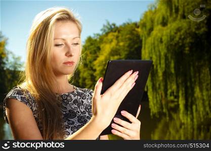 Technology, outdoor relaxation concept. Woman in park, relaxing and using tablet, ebook spending her leisure time outside. Woman sitting in park, relaxing and using tablet