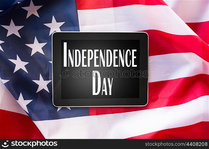 technology, patriotism, anniversary, national holidays and celebration concept - close up of tablet pc computer on american flag and independence day words on screen
