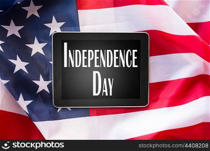technology, patriotism, anniversary, national holidays and celebration concept - close up of tablet pc computer on american flag and independence day words on screen