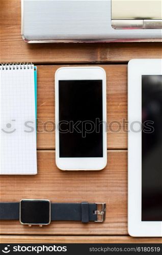 technology, people and advertisement concept - close up of smartphone and smartwatch with screen and office supplies on wooden table