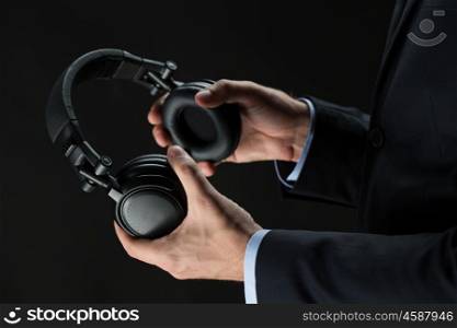 technology, people and business concept - close up of businessman hands holding headphones over black background