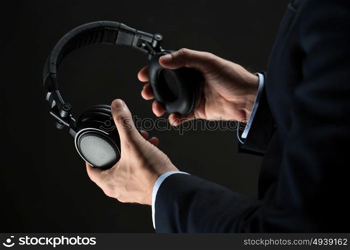 technology, people and business concept - close up of businessman hands holding headphones over black background. close up of businessman hands holding headphones