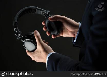 technology, people and business concept - close up of businessman hands holding headphones over black background. close up of businessman hands holding headphones