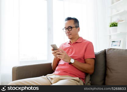 technology, people and communication concept - asian man with smartphone sitting on sofa at home. asian man with smartphone sitting on sofa at home