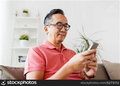 technology, people and communication concept - asian man with smartphone sitting on sofa at home. asian man with smartphone sitting on sofa at home