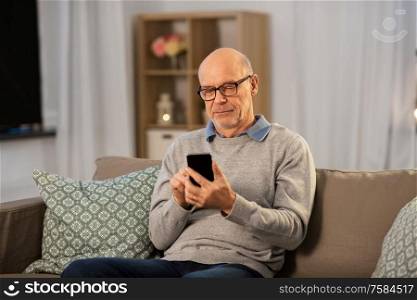 technology, people and communication concept - bald senior man texting on smartphone at home in evening. senior man texting on smartphone at home