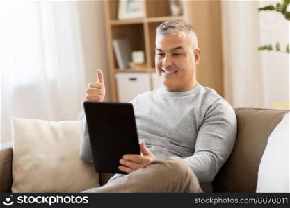 technology, people and communication concept - happy man with tablet pc computer having video chat at home and showing thumbs up. man having video chat on tablet pc at home. man having video chat on tablet pc at home