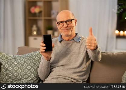 technology, people and communication concept - happy smiling bald senior man with smartphone showing thumbs up at home in evening. happy senior man with smartphone at home