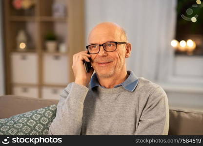 technology, people and communication concept - happy smiling senior man calling on smartphone at home in evening. happy senior man calling on smartphone at home