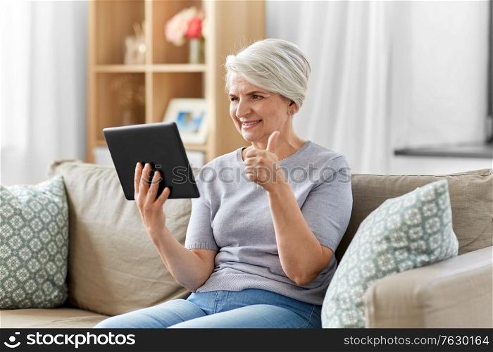 technology, people and communication concept - happy smiling senior woman with tablet pc computer having video call at home and showing thumbs up. senior woman having video chat on tablet pc