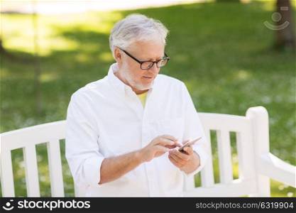 technology, people and communication concept - senior man dialing number or networking on smartphone at summer park. senior man with smartphone at summer park