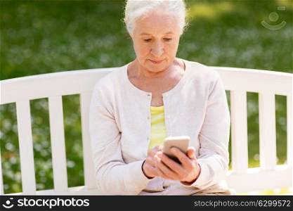 technology, people and communication concept - senior woman messaging or networking on smartphone at summer park. senior woman with smartphone at summer park