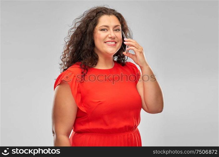 technology, people and communication concept - smiling woman in red dress calling on smartphone over grey background. smiling woman in red dress calling on smartphone