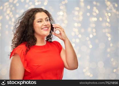 technology, people and communication concept - smiling woman in red dress calling on smartphone over festive lights background. smiling woman in red dress calling on smartphone